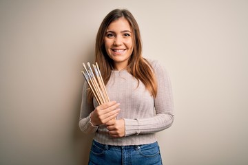 Poster - Young painter artist woman painting using paintbrush over isolated background with a happy face standing and smiling with a confident smile showing teeth