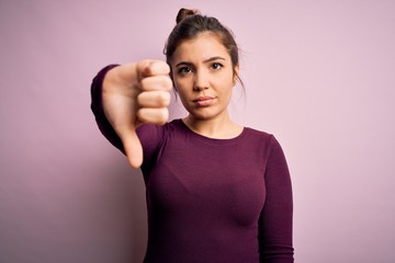 Sticker - Beautiful young woman wearing casual bun hairstyle over pink isolated background looking unhappy and angry showing rejection and negative with thumbs down gesture. Bad expression.