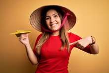 Tourist Woman Wearing Traditional Asian Rice Paddy Straw Hat Holding Paper Plane For A Trip With Surprise Face Pointing Finger To Himself
