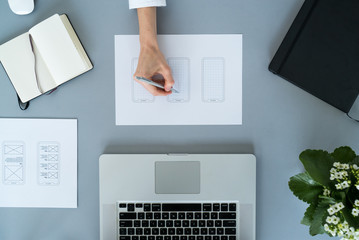 Web designer at work. Graphic designer. Mobile application design. Designer desk. UX, UI design. Thumbnails of a mobile application sketches. Laptop, sketchbook, pencil on the table.