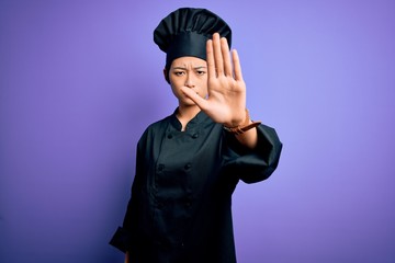 Young beautiful chinese chef woman wearing cooker uniform and hat over purple background doing stop sing with palm of the hand. Warning expression with negative and serious gesture on the face.