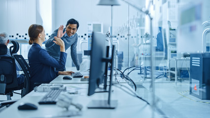 Poster - Inside Factory Office: Male Project Supervisor Talks to a Female Industrial Engineer who Works on Computer, Give High Five. In Workshop: Workers Use High-Tech Industry 4 CNC Machinery, Robot Arm.