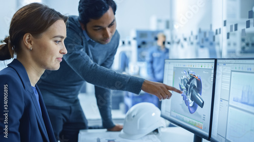 In Factory Workshop: Professional Workers Use High-Tech Industrial CNC Machinery, Robot Arm. Inside Office: Male Project Supervisor Talks to a Female Industry 4 Engineer who Works on Computer, Talk