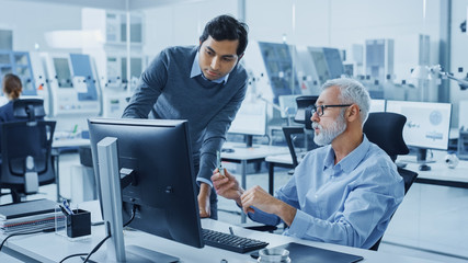Poster - Modern Factory Office: Indian Project Manager Talks to Caucasian Senior Engineer whos Working on Computer, Inspect Metal Component. Professionals Solving Heavy Industry Problems, Having Discussion 