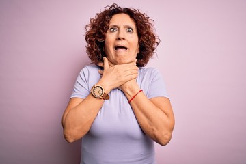 Canvas Print - Middle age beautiful curly hair woman wearing casual t-shirt over isolated pink background shouting and suffocate because painful strangle. Health problem. Asphyxiate and suicide concept.