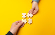 © Andrii Zastrozhnov - Two hands connect puzzles on a yellow background. Cooperation and teamwork in business. Collaboration people for success.