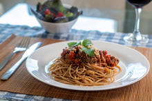 
wholemeal spaghetti pasta with bolognese sauce and basil on a white plate