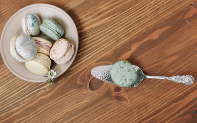 Wall Mural - Colorful homemade macarons are lying on theplate on the brown wooden background. Envelope with blossom.