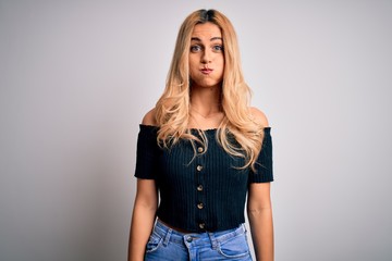 Poster - Young beautiful blonde woman wearing casual t-shirt standing over isolated white background puffing cheeks with funny face. Mouth inflated with air, crazy expression.