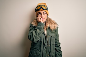 Canvas Print - Young brunette skier woman wearing snow clothes and ski goggles over white background looking stressed and nervous with hands on mouth biting nails. Anxiety problem.