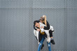 © LUCIA VARGAS/ADDICTIVE STOCK - Overjoyed black haired lay in stylish casual wear laughing while giving girlfriend piggyback ride against grey wall of building