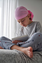 From Below Serious Child With Cancer Diagnosis Making Notes While Sitting On Bed In Room