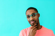 © Carlos David - Portrait of a young man with glasses thinking, deciding and holding his chin, against blue studio background