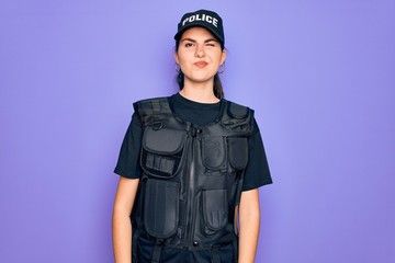 Poster - Young police woman wearing security bulletproof vest uniform over purple background winking looking at the camera with sexy expression, cheerful and happy face.