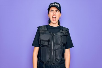 Poster - Young police woman wearing security bulletproof vest uniform over purple background angry and mad screaming frustrated and furious, shouting with anger. Rage and aggressive concept.