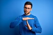 Young handsome man with beard wearing casual sweater and glasses over blue background Doing time out gesture with hands, frustrated and serious face