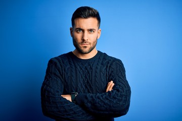 Young handsome man wearing casual sweater standing over isolated blue background skeptic and nervous, disapproving expression on face with crossed arms. Negative person.