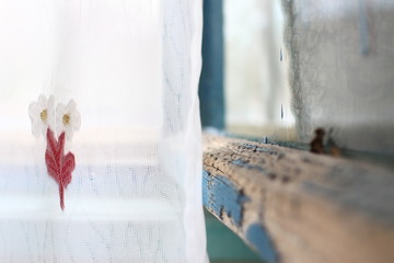 old wooden glazed window frame with peeling paint and white transparent tulle with flowers