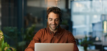 Smiling Businessman Talking On A Headset And Using A Laptop
