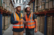 © StratfordProductions - Young sacred workers in warehouse discussing work on digital tablet looking away towards goods on shelf