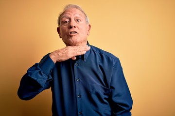 Wall Mural - Grey haired senior man wearing casual blue shirt standing over yellow background cutting throat with hand as knife, threaten aggression with furious violence