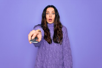 Young beautiful woman using television remote control over isolated purple background scared in shock with a surprise face, afraid and excited with fear expression