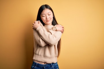 Sticker - Young beautiful asian woman wearing casual sweater over yellow isolated background Hugging oneself happy and positive, smiling confident. Self love and self care