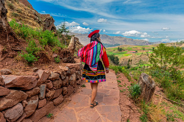 Quechua Indigenous Woman in traditional clothes walking along ancient Inca Wall in the ruin of Tipon, Cusco, Peru.