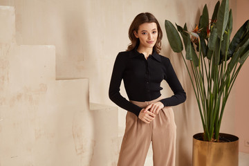 Wall Mural - Beautiful brunette woman natural make up wear fashion clothes casual dress code office style black blouse and beige pants suit for romantic date business meeting accessory interior stairs flowerpot.