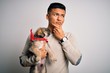 © Krakenimages.com - Young handsome latin man holding cute puppy pet over isolated white background serious face thinking about question, very confused idea