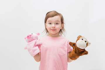 Wall Mural - A little girl with toys on her hands on a white background with an open seat. Cute Girl playing with toys in the hands of a Puppet theater.Toys in the form of a monkey and a pig