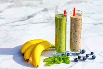 2 different kind of banana based smoothies with ingredients on marble table background .