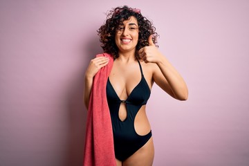 Sticker - Young beautiful curly arab woman on vacation wearing swimsuit holding beach towel happy with big smile doing ok sign, thumb up with fingers, excellent sign