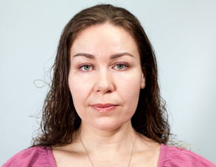 Portrait of a woman with long curly hair with a neutral expression, grey background, emotions series.