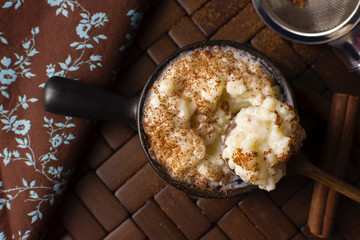 Spoon of traditional June party Brazilian dessert made of rice and condensed milk called arroz doce decorated with cinnamon in wood background seen from above