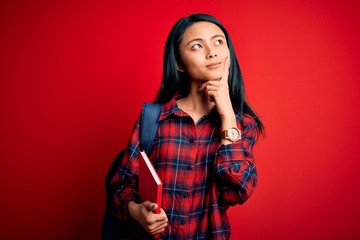 Wall Mural - Young beautiful chinese student woman holding book standing over isolated pink background serious face thinking about question, very confused idea