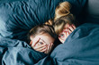© stakhov - Portrait of light hair long hair mother and daughter under the duvet together in soft morning light on blue linen bed. Concept of happy family living, relaxation, comfort, fun. Play hide and seek