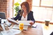 © Krakenimages.com - Middle age beautiful businesswoman smiling happy and confident. Sitting on chair working in a desk reading documents at the office
