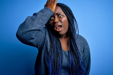 Poster - African american plus size woman with braids wearing casual sweater over blue background surprised with hand on head for mistake, remember error. Forgot, bad memory concept.