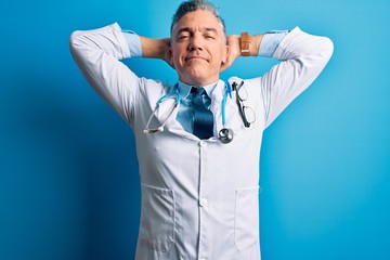 Poster - Middle age handsome grey-haired doctor man wearing coat and blue stethoscope relaxing and stretching, arms and hands behind head and neck smiling happy