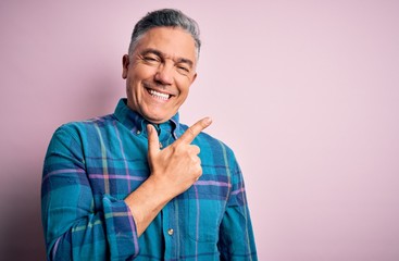 Wall Mural - Middle age handsome grey-haired man wearing casual shirt over isolated pink background cheerful with a smile of face pointing with hand and finger up to the side with happy and natural expression