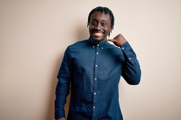 Poster - Young handsome african american man wearing casual shirt standing over white background smiling doing phone gesture with hand and fingers like talking on the telephone. Communicating concepts.