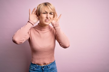 Sticker - Young blonde woman with short hair wearing casual turtleneck sweater over pink background Trying to hear both hands on ear gesture, curious for gossip. Hearing problem, deaf