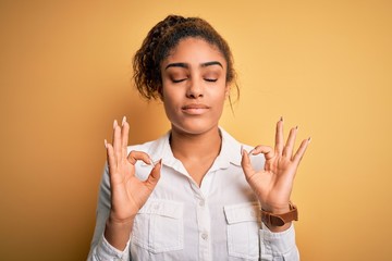 Wall Mural - Young beautiful african american girl wearing casual shirt standing over yellow background relax and smiling with eyes closed doing meditation gesture with fingers. Yoga concept.