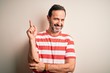 © Krakenimages.com - Middle age hoary man wearing casual striped t-shirt standing over isolated white background with a big smile on face, pointing with hand and finger to the side looking at the camera.