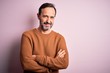 © Krakenimages.com - Middle age hoary man wearing casual brown sweater standing over isolated pink background happy face smiling with crossed arms looking at the camera. Positive person.
