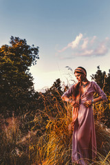 Wall Mural - beautiful young fashionable woman in dress on the field at sunset