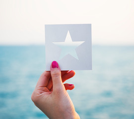 Wall Mural - Hand holding perforated paper star shape with ocean background