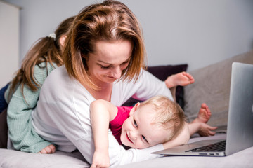 Wall Mural - Young women works at home with laptop along with two children.Children want to communicate with mother, make noise and interfere with work.Self-isolation during coronovirus pandemic