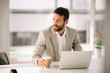 © JustLife - Businessman drinking coffee in office. Handsome man working on lap top.